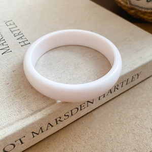 Close-up of a smooth white resin round bangle resting on a vintage art book