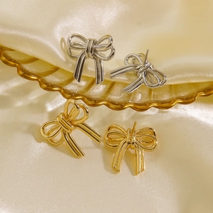 Elegant gold and silver bow stud earrings with polished finish on silk background