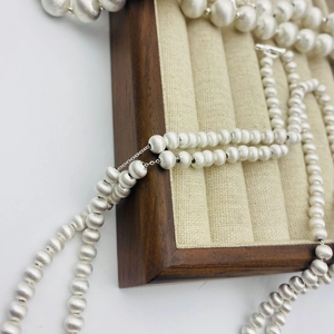Gros plan d'un collier à perles argent mat sur un plateau à bijoux texturé détail