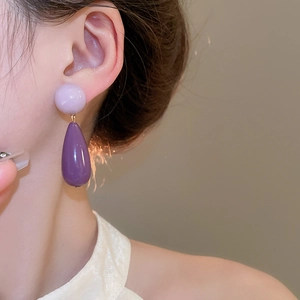 Detailed macro view of purple acrylic teardrop earrings worn by a model in soft lighting