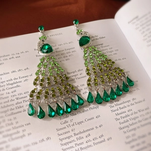 Detailed macro of emerald crystal peacock tassel earrings on a vintage book background