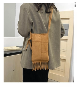 Close-up of brown suede hobo bag with long fringes styled on a grey blazer outfit