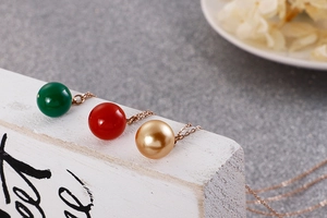 Vue détaillée des colliers à pendentif perle en vert, rouge et or sur bois