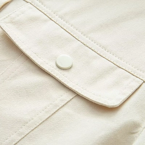 Detailed close-up of cream cotton twill fabric with a round button and pocket flap detail