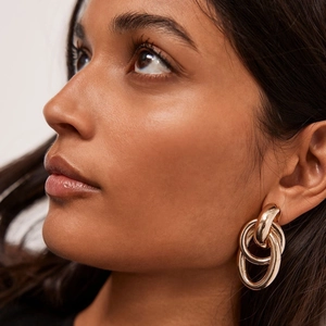 Macro shot of 18k gold interlocking triple hoop earrings on model showing modern gloss