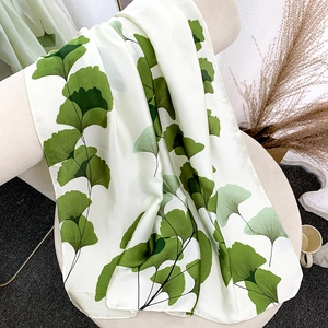 Écharpe en soie blanche avec motifs feuilles de ginkgo vert drapée sur chaise pour la plage