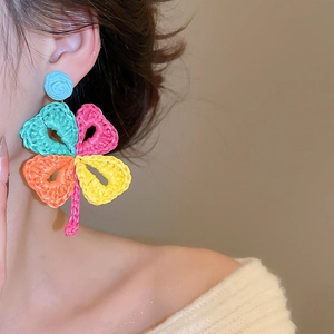 Close-up of woven raffia clover earrings with colorful petals on model for vacation