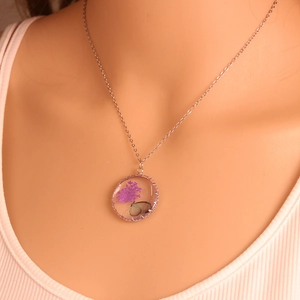Close-up of bohemian silver necklace featuring round glass pendant with purple dried flowers