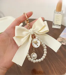 Close-up of cream bow keychain with pearl ring and gold fashion trend coin pendant
