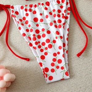 Detail of high-waisted white bikini bottom with red berry print and side tie strings