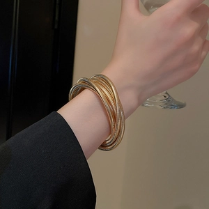 Detail of elegant gold multi-layer spring cuff bracelet on wrist with a black sleeve