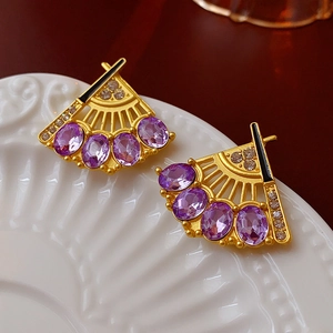 Macro view of vintage gold fan earrings with purple gems and crystals on a white plate