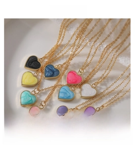 Colorful enamel heart pendants on gold chains arranged in a ceramic dish