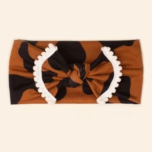 Close-up of baby leopard print headband with a soft bow and white pom-pom trim detail