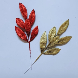 Dettaglio di foglie di pino artificiali glitterate rosse e oro per decorazioni natalizie