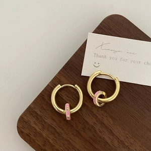 Detail of gold hoops with pink enamel centers on a textured wooden surface