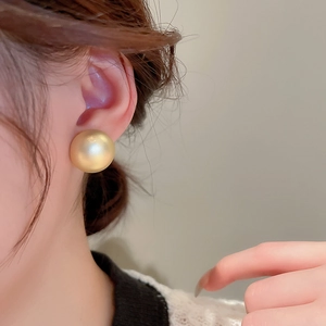 Macro detail of large matte gold hemispherical stud earring on model with satin finish