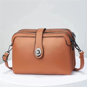Detail view of brown pebbled leather crossbody bag with triple zippers and metal clasp