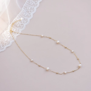 Close-up of a gold pearl necklace with small white pearls and lace background decor
