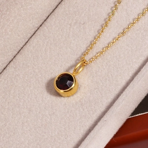 Close-up of golden necklace with a round deep red birthstone pendant in a jewelry box
