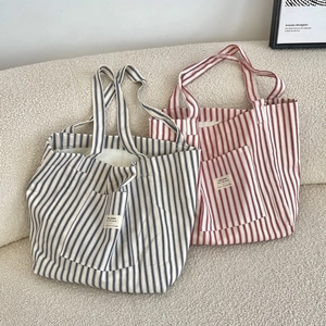 Blue and red striped canvas tote bags displayed on a beige sofa in a minimalist setting