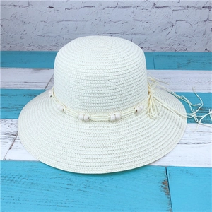 Close-up of cream woven straw sun hat featuring decorative wood beads and long tassels