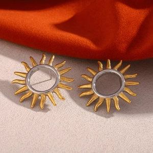 Close-up of two-tone hollow sun stud earrings in gold and silver over a beige surface