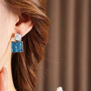 Detail of square blue and white enamel earrings with hammered texture on a model