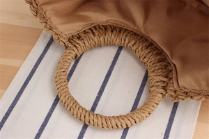 Detailed view of natural straw woven bag with circular handles and brown fabric lining