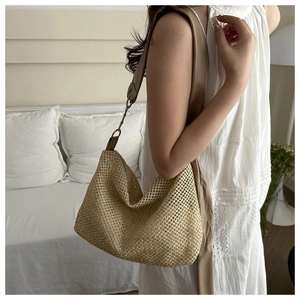 Detail of light beige woven tote bag with a wide brown leather strap on a model
