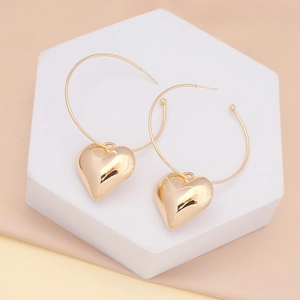 Detailed close-up of gold heart pendant hoop earrings on a white geometric platform