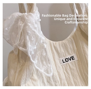 Detail of cream tote bag featuring textured fabric, LOVE patch, and large lace bow