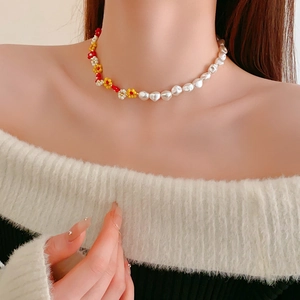 Close-up of pearl necklace with red and yellow beaded flowers on female model neck
