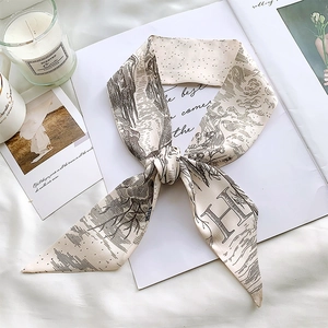 Detail of a vintage cream silk scarf with 'H' print on a white fabric and book background