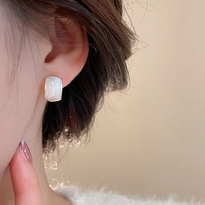 Close-up of elegant gold rectangular pearl stud earrings worn with a beige knitted sweater