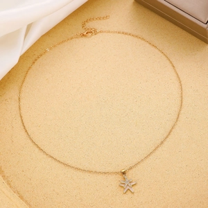Dettaglio della collana con ciondolo a stella marina dorata e zirconi su sfondo in raso