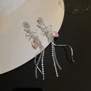 Detail of silver long tassel earrings with pink heart stones and bow accents on mirror