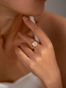Detailed view of a gold chain ring with square mother of pearl inlay worn on a finger