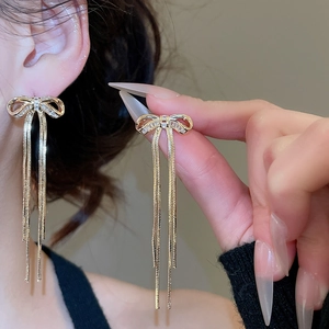 Makroaufnahme eleganter goldener Schleifen-Ohrringe mit Zirkon-Steinen und Quasten