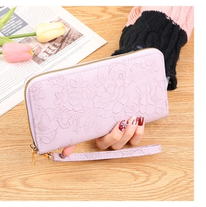 Pink zip-around wallet with embossed floral design and wristlet held over wooden table