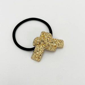 Detailed macro view of the gold cross charm with hammered texture on black elastic hair tie
