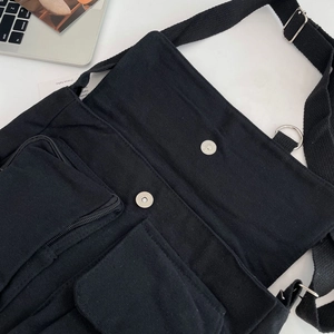 Close-up of black canvas crossbody bag featuring multi-pocket design and silver metal buckle