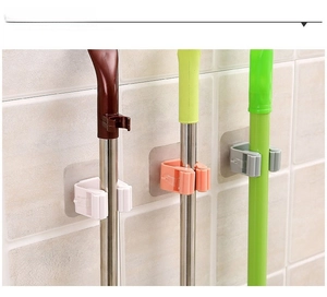 Three adhesive wall mop holders in white pink and gray on a tiled bathroom wall