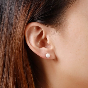 Elegant white round pearl stud earrings in stainless steel on a female model