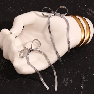 Close-up of silver bow tassel earrings displayed on a white hand-shaped jewelry stand