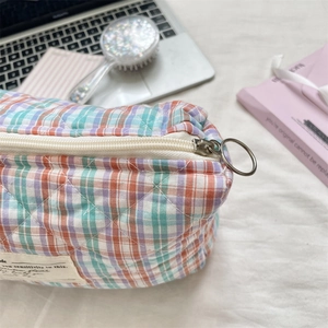 Detail of checkered quilted cosmetic bag with metal ring zipper on textured background