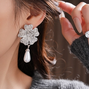 Close-up of silver flower earrings with pave rhinestones and a teardrop pearl drop