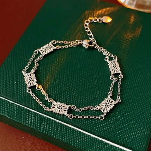 Detail of silver double-layer bracelet with floral charms on a green gift box