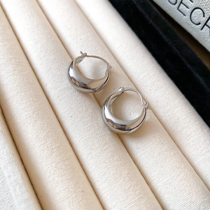 Detailed close-up of chunky silver drop hoop earrings on a beige textured jewelry tray