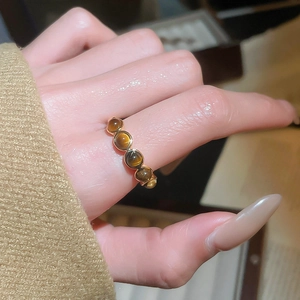 Détail d'une bague dorée ornée de cinq pierres œil de tigre rondes sur l'index